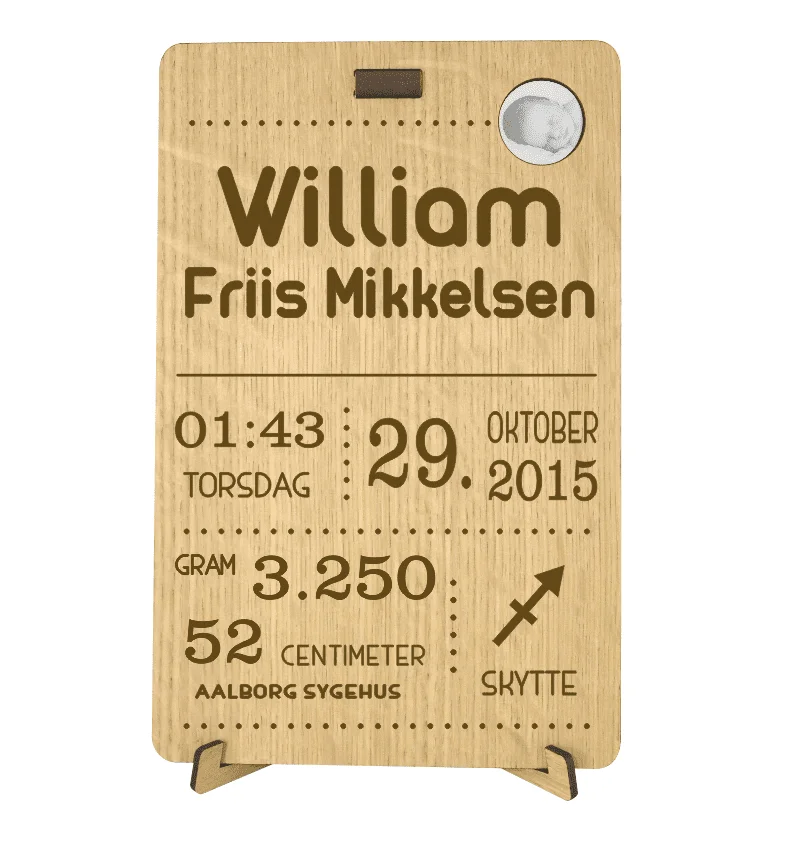 Personlig fødselstavle i egetræsfiner med gravering af navn 'William Friis Mikkelsen', fødselsdata, og babyfoto.